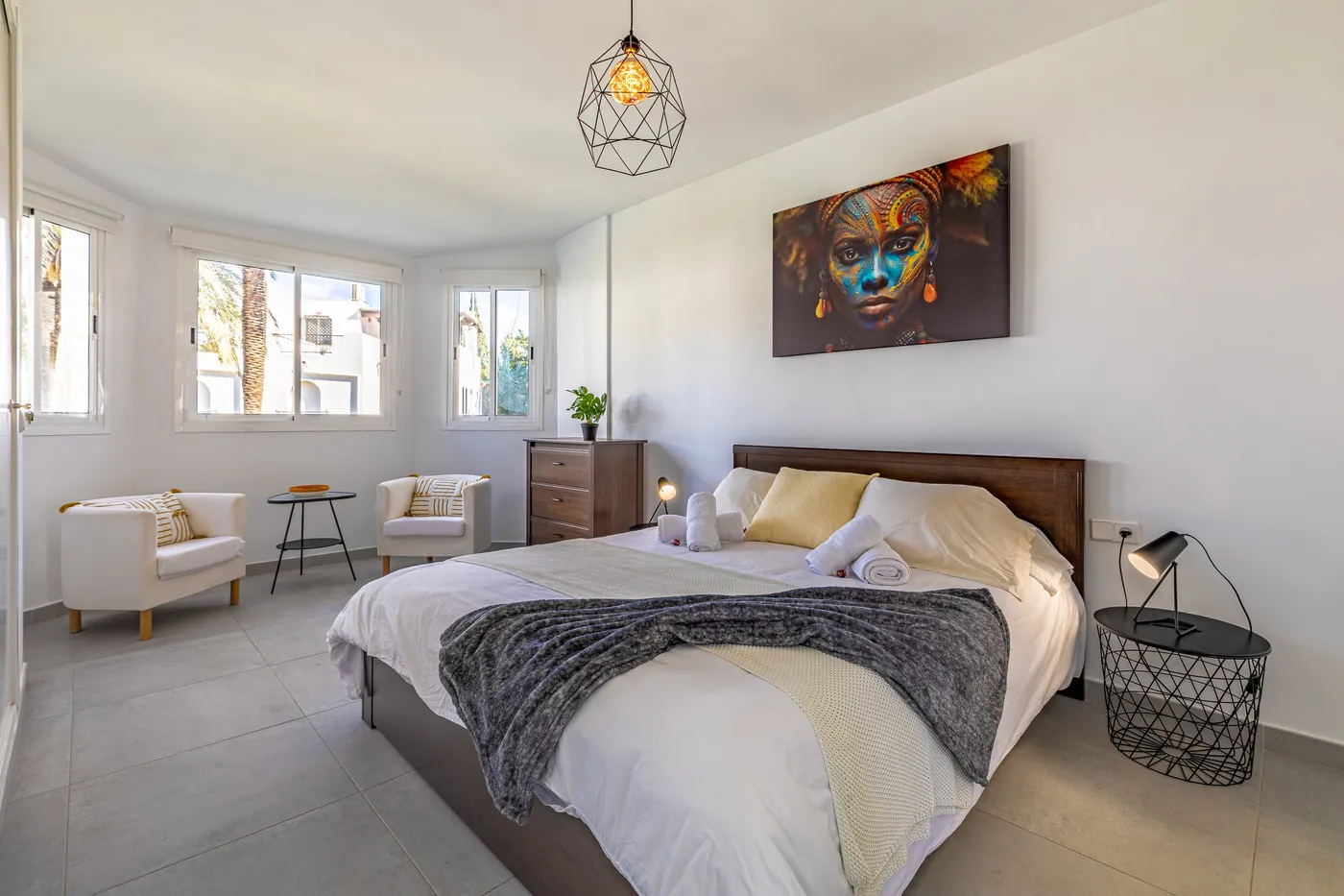 El mismo dormitorio después: ropa de cama nueva, una manta, lámparas de noche y un gran cuadro.