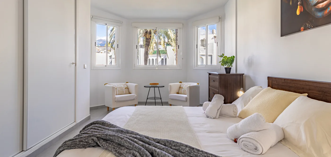 A freshly made master bedroom, linen crisp and towels rolled, prepared before an arrival.